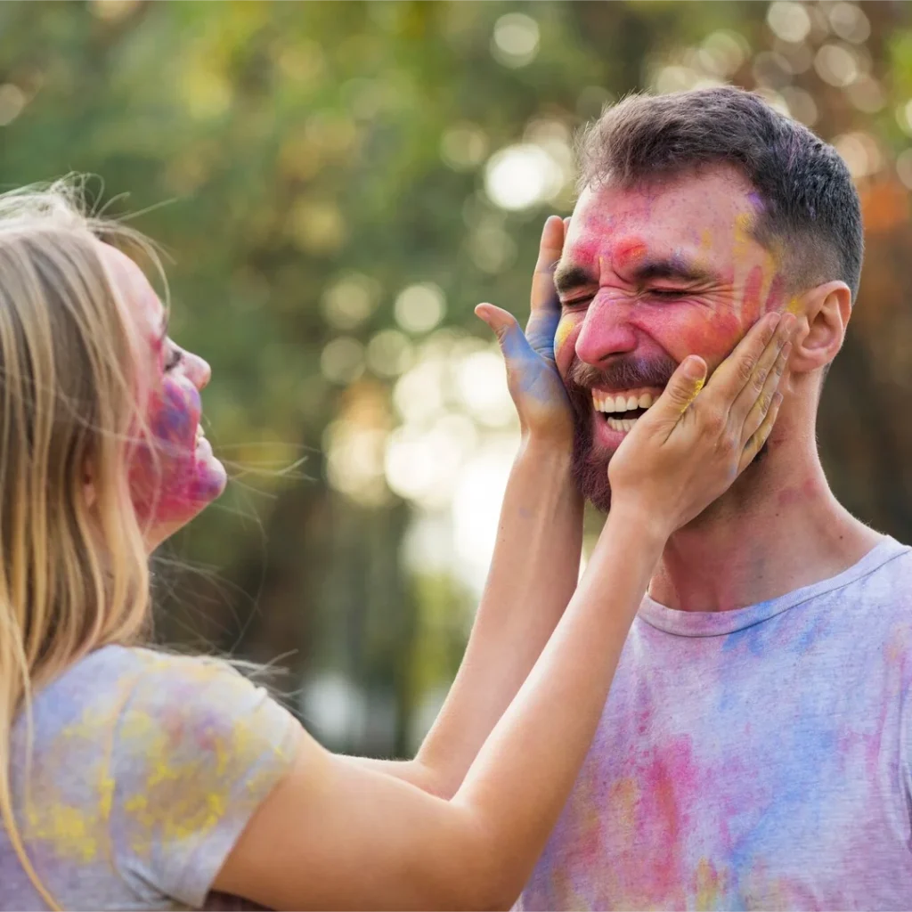 Person applying natural color on another person’s cheek during Holi celebration